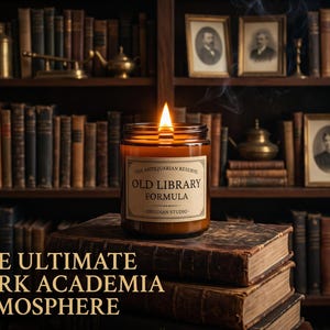 Könnte beinhalten: Eine brennende Kerze im bernsteinfarbenen Glas mit einem Etikett, auf dem THE ANTIQUARIAN RESERVE OLD LIBRARY FORMULA OBSIDIAN STUDIO steht, platziert auf einem Stapel alter ledergebundener Bücher. Die Flamme leuchtet vor einem dunklen Bücherregal.