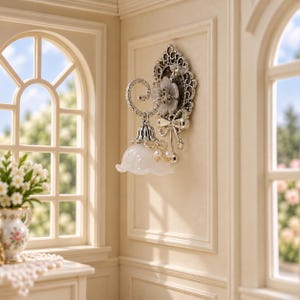 May include: A miniature wall-mounted lamp featuring a silver-toned ornate backplate with a bow detail, a curved arm, and a bell-shaped white glass shade. The fixture is accented with small white pearls and a delicate floral motif.