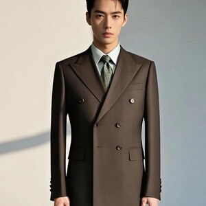 May include: A dark brown double-breasted suit jacket with wide lapels and four visible buttons, worn over a light green collared dress shirt and a dark green patterned necktie. The jacket features structured shoulders and two side pockets.