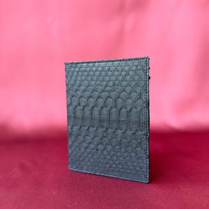 May include: A rectangular card holder wallet featuring a dark charcoal grey exterior with a distinct, raised scale texture pattern. The item is constructed with visible stitching along the edges, maintaining a slim, upright, and structured profile.