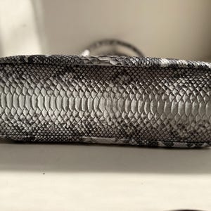 May include: A rectangular handbag base featuring a monochromatic snakeskin pattern in shades of gray, black, and white. The surface displays a textured, overlapping scale design with a distinct central panel of larger scales and smaller scales on the sides.