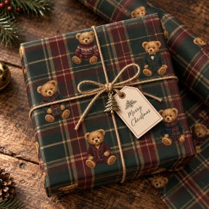 May include: A square gift box wrapped in dark green and red plaid paper featuring illustrations of teddy bears in various outfits. The box is tied with brown twine and includes a beige gift tag with the text Merry Christmas.