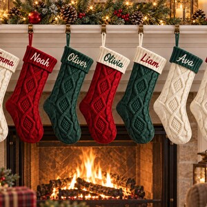 May include: Seven cable-knit Christmas stockings hanging in a row, featuring alternating red, green, and cream colours. Each stocking has a personalised cuff embroidered with the names Emma, Noah, Oliver, Olivia, Liam, Ava, and Sophie in script font.