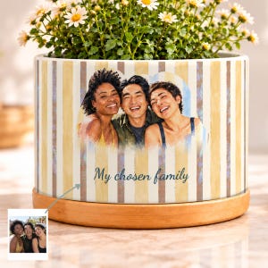 May include: A cylindrical ceramic planter with a light yellow and white vertical striped pattern. The front features a printed photograph of three smiling people and the text My chosen family. A wooden base sits beneath the planter.