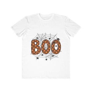 May include: A white short-sleeve t-shirt featuring a central graphic of the word BOO in brown with orange polka dots. The letters are layered over a black spiderweb design with several small black spiders crawling on the web and the letters.