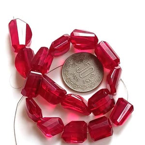May include: A strand of translucent, faceted, deep red beads arranged in a circular pattern. A circular 50 paise coin from 1985 is placed in the center of the beads for scale, showing the text 50 PAISE and the year 1985 on its metallic surface.