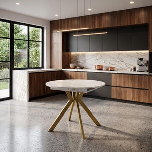 May include: A round dining table with a white marble-patterned top and four angled gold-toned metal legs. The table is positioned in a kitchen featuring dark wood and matte black cabinetry, a white marble backsplash, and a large window.