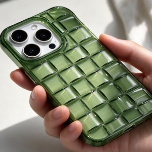 Op de afbeelding: Een doorschijnend olijfgroen smartphonehoesje met een verhoogd, driedimensionaal rasterpatroon van vierkante, kussenachtige segmenten. Het hoesje heeft een glanzende afwerking en een uitsparing voor een camera met drie lenzen.
