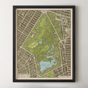 May include: A framed map print of Prospect Park in Brooklyn, featuring a detailed top-down view of the park's green spaces, winding paths, and the Prospect Park Lake in light blue, all enclosed within a simple black frame on a white wall.