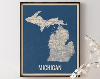 May include: A framed wall art print featuring a detailed map of the state of Michigan in beige against a dark blue background. The map displays intricate road networks and geographical outlines. The word MICHIGAN is printed in bold beige capital letters.