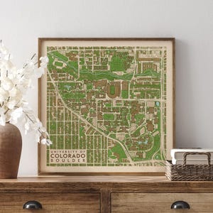 May include: A square framed map print of the University of Colorado Boulder campus. The map features a detailed layout of buildings and green spaces in shades of green and brown, with the text University of Colorado Boulder in the corner.