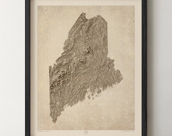 May include: A framed topographic map of the state of Maine featuring a textured, relief-style brown terrain illustration set against a light beige background. The print is enclosed in a thin black frame with small text at the bottom center.