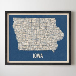 May include: Framed map print of Iowa, featuring a detailed road network in a cream color against a deep blue background. The word "IOWA" is printed in white at the bottom. The print is encased in a black frame.