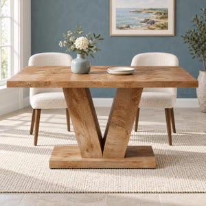 Può includere: Un tavolo da pranzo rettangolare in legno marrone chiaro con una base a piedistallo a forma di V, caratterizzato da una venatura del legno naturale. Due sedie imbottite color crema con gambe in legno sono posizionate ai lati.