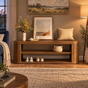 May include: A long, oval-shaped wooden hallway bench featuring a smooth top surface, a middle shelf, and an open bottom section. The bench has vertical slat detailing on the rounded ends and is finished in a warm, medium-toned wood stain.