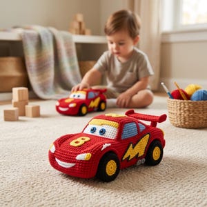 Può includere: Un'auto giocattolo all'uncinetto rossa con un fulmine giallo sul lato, un numero 8 giallo sul cofano, finestrini blu e uno spoiler posteriore. L'auto ha ruote nere con centri gialli, fari bianchi e una bocca sorridente.
