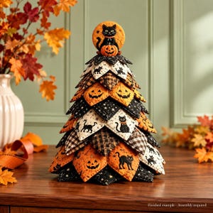 May include: A decorative fabric tree featuring a quilted pattern with Halloween motifs including black cats, jack-o'-lanterns, stars, and plaid designs. The tree is topped with a circular ornament showing a black cat sitting on a pumpkin.