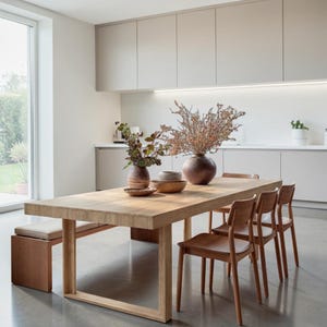 May include: A rectangular light wood dining table with a matching bench and three wooden chairs. On the table are two ceramic vases containing dried branches and a small wooden bowl. The furniture is set in a kitchen with light gray cabinets.