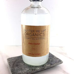 May include: A clear glass bottle with a brown label that reads "Butter Me Up Organics, a modern day apothecary, Glass Cleaner, Lime, 16 fl. oz / 473 ml".
