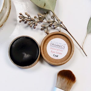 Puede incluir: Un pequeño recipiente redondo de delineador de ojos negro con el texto "BUTTER ME UP" ORGANICS Chemical Free Eye Liner Coal 33 oz/8 g" en la tapa. Un pincel está al lado del recipiente.