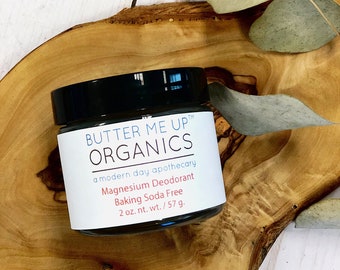 May include: A white jar with a black lid and a label that reads "BUTTER ME UP™ ORGANICS a modern day apothecary Magnesium Deodorant Baking Soda Free 2 oz. nt. wt./57 g."