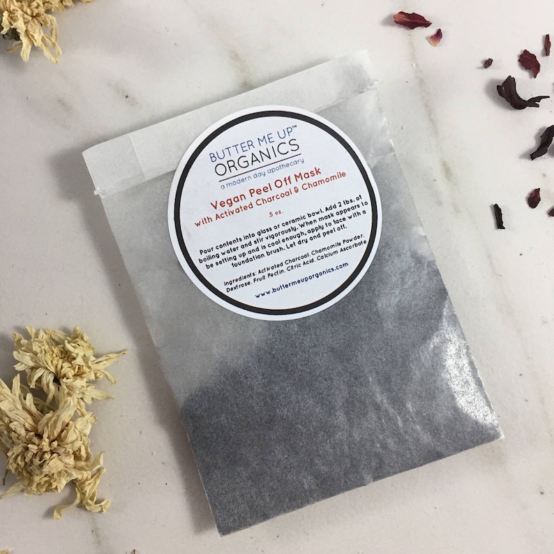May include: A white paper pouch with a black powder inside. The pouch has a sticker on the front that says "Butter Me Up Organics" and "Vegan Peel Off Mask with Activated Charcoal & Chamomile".