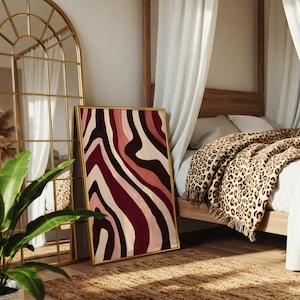 May include: A rectangular framed wall art piece featuring an abstract pattern of flowing, wavy vertical stripes in shades of deep burgundy, soft blush pink, and cream. The artwork is encased in a thin gold-toned metal frame with a smooth finish.