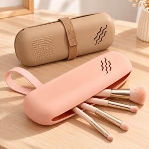 Peut inclure: Deux étuis en silicone allongés et arrondis pour pinceaux de maquillage, l'un beige et l'autre rose clair. L'étui beige présente un motif texturé en forme de drapeau et des lignes ondulées. L'étui rose a une sangle et contient quatre pinceaux.