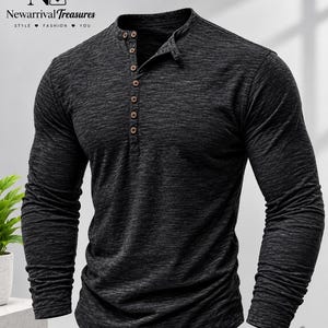 May include: A long-sleeve henley shirt in a dark charcoal gray heathered fabric. The shirt features a mandarin collar and a partial front placket with six small, round, light brown buttons. The fabric has a subtle, textured, mottled appearance.