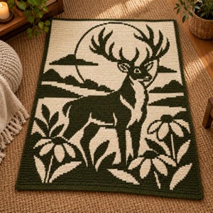 May include: A rectangular crochet blanket featuring a dark forest green and cream color scheme. The design depicts a large stag standing in a field of flowers with a full moon and mountain silhouette in the background, created with a pixelated pattern.