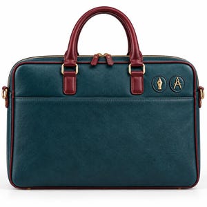 Puede incluir: Un maletín de color verde azulado oscuro con ribetes y asas de color rojo intenso. El bolso cuenta con herrajes dorados, incluyendo dos cremalleras y dos emblemas metálicos circulares en la parte frontal, uno con una pluma y otro con un compás.