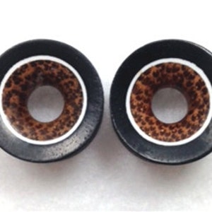 May include: Pair of black wood ear gauges with a white ring and brown wood inlay.