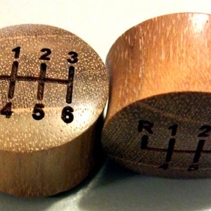 May include: Two wooden gear shift knobs with a 6-speed pattern engraved on the top. The knobs are brown and have a natural wood grain.