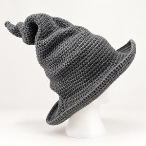 May include: A dark gray crocheted hat with a tall, pointed, and slightly curved crown. The hat features a wide, circular brim and a textured, yarn-based construction throughout, showcasing a consistent stitch pattern in a solid dark gray color.