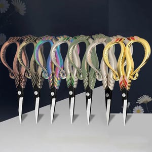 May include: A row of seven decorative scissors with ornate, swan-shaped handles in various metallic finishes including copper, bronze, iridescent rainbow, silver, sage green, white, and gold with red accents, all featuring sharp steel blades.