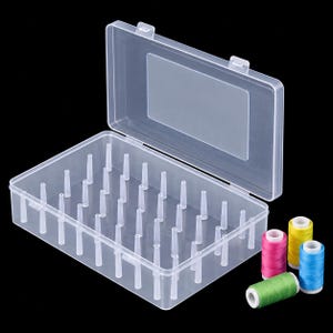 May include: A clear plastic storage box with a hinged lid and multiple vertical pegs inside for organizing thread spools. Four small spools of sewing thread in yellow, pink, blue, and green are positioned outside the open container.