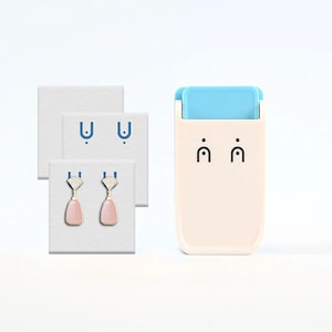 May include: A pair of drop earrings featuring pink teardrop-shaped stones suspended from silver-toned fan-shaped tops with clear accents. The earrings are displayed on a white square card next to a rectangular beige device with a light blue top.