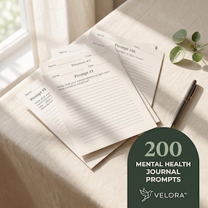 May include: A stack of off-white paper sheets featuring printed journal prompts with lines for writing. Each sheet includes fields for Name and Date. One sheet displays Prompt #1, another Prompt #16. A dark green arch-shaped graphic displays 200 MENTAL HEALTH JOURNAL PROMPTS and the text VELORA.