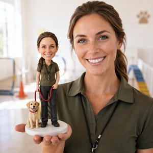 May include: A custom bobblehead figurine featuring a person with brown hair wearing an olive green polo shirt and dark trousers, holding a red leash attached to a light-colored dog. The figurine stands on a circular white base.