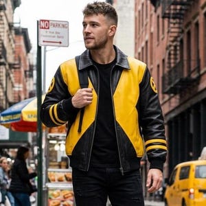 Può includere: Una giacca in pelle nera e gialla con colletto a punta, chiusura frontale con zip e polsini a coste con due strisce gialle. Le maniche presentano emblemi circolari gialli e neri, e i pannelli sul petto sono di colore giallo brillante.