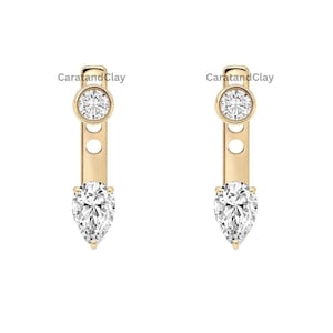 May include: A pair of gold earrings featuring a vertical bar design with a round brilliant-cut stone at the top and a pear-shaped stone at the bottom. Each earring includes the text CaratandClay printed near the top round stone setting.