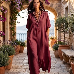May include: A dark rose-colored midi-length dress with a collared neckline, short sleeves, and side pockets. The dress is paired with a layered beaded necklace, gold-toned drop earrings, and brown leather sandals with a strappy design.