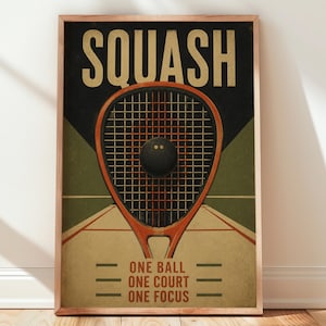 May include: A framed poster featuring a squash racket and ball centred over a court graphic. The text SQUASH appears at the top in large beige letters, while the bottom text reads ONE BALL, ONE COURT, ONE FOCUS in a dark red font.