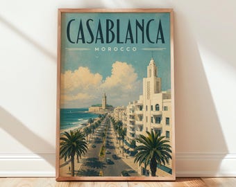 May include: A framed vertical travel poster featuring a coastal city scene in Casablanca, Morocco. The artwork displays a street lined with palm trees, white buildings, and a distant mosque by the sea under a blue sky with white clouds.