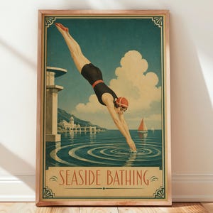 Op de afbeelding: Een rechthoekige ingelijste poster met een vintage-stijl illustratie van een persoon in een zwart badpak en rode badmuts die in blauw water duikt. De tekst SEASIDE BATHING staat onderaan. Een duikplank, gebouwen in de verte en een zeilboot.