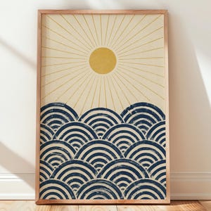 Puede incluir: Una impresión de arte mural rectangular enmarcada que presenta un sol amarillo con líneas finas radiantes sobre una serie de patrones de olas semicirculares de color azul oscuro sobre un fondo crema claro en un marco de madera.