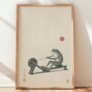 May include: A framed art print featuring a detailed black ink illustration of a frog using a rowing machine. The background is a light cream color with vertical line textures, a small red circle, and Japanese characters in the lower left corner.