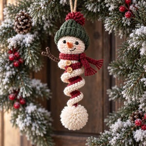 May include: A crocheted snowman ornament featuring a dark green knit hat with a red pom-pom, a red scarf, and two small wooden buttons on its chest. The snowman has a spiral-shaped body in white and red, ending in a large white pom-pom.