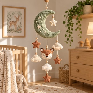 Può includere: Una giostrina sospesa per la cameretta con una grande mezzaluna all'uncinetto color verde salvia decorata con piccole stelle bianche. Dalla luna pendono elementi all'uncinetto tra cui un muso di volpe, nuvole color crema e stelle color ruggine, collegati da fili bianchi e piccole perline di legno.