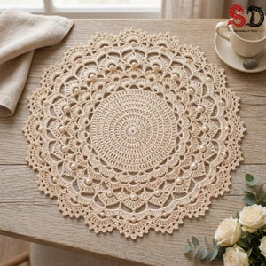 May include: A round, cream-colored crochet doily featuring an intricate, radiating pattern of concentric circles and scalloped edges. The design is embellished with small, round, white faux pearls integrated into the delicate yarn structure.